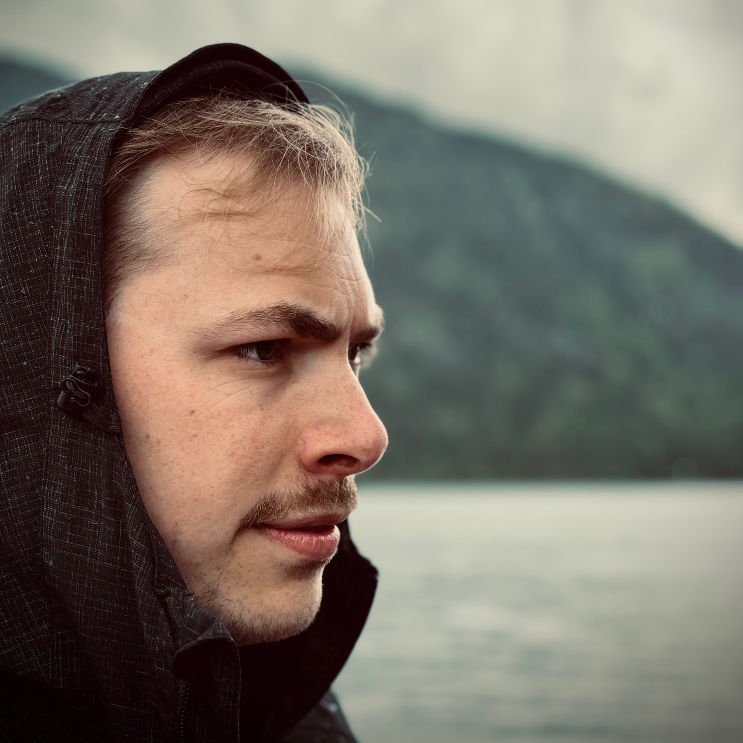 Jacob contemplating, looking in the distance, with a black hood on the head, in a rainy dark scenery.